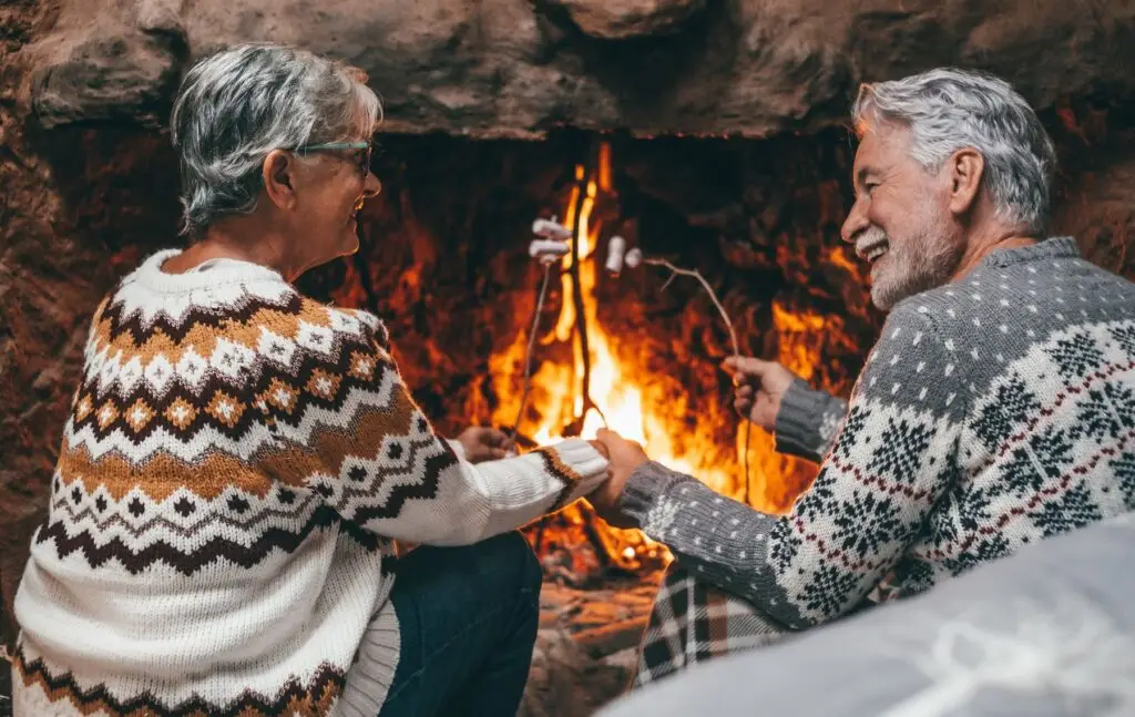 Older couple roast marshmallows by a cozy fireplace during winter at Covenant Woods in Columbus, GA.
