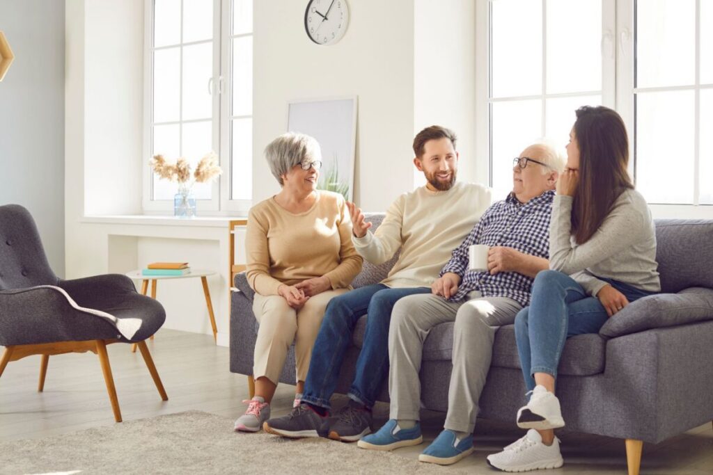 Older adults and their adult children having a warm conversation in a bright living room, illustrating how to talk to a parent about assisted living